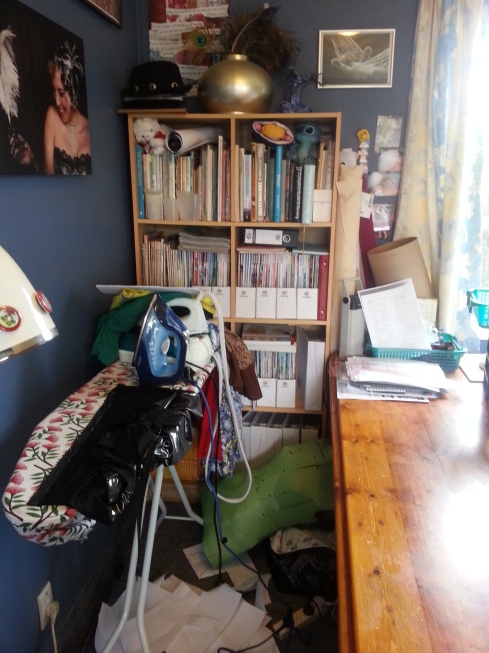 The other corner, opposite from the sewing cupboard. My shelves, filled with sewing and crafting books, knitting magazines, and Burda magazines; and my ironing board, currently drowning in undone ironing. Pressing in a project, yes. Ironing my washing, very infrequently. 